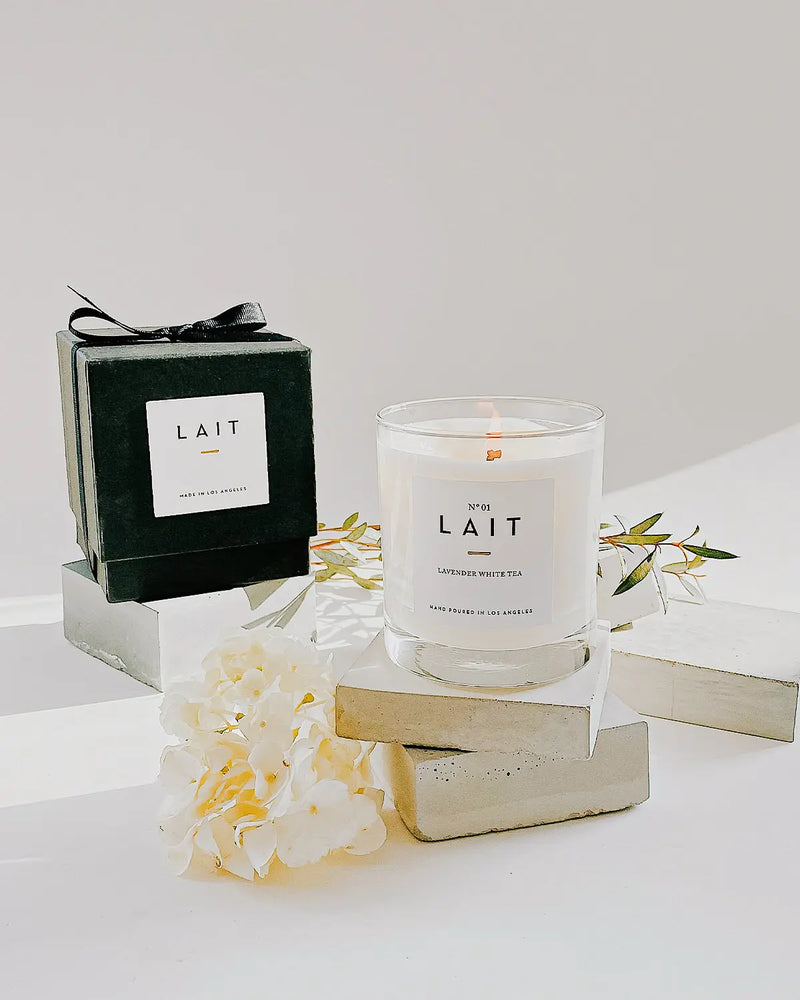 A beautiful photo of one lit candle and elegant black gift box styled with white photos and cement stands.